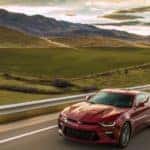 Red 2016 Chevrolet Camaro sports car driving on a paved road next to mountains