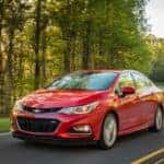 Red 2016 Chevrolet Cruze sedan on a paved road next to tall green trees