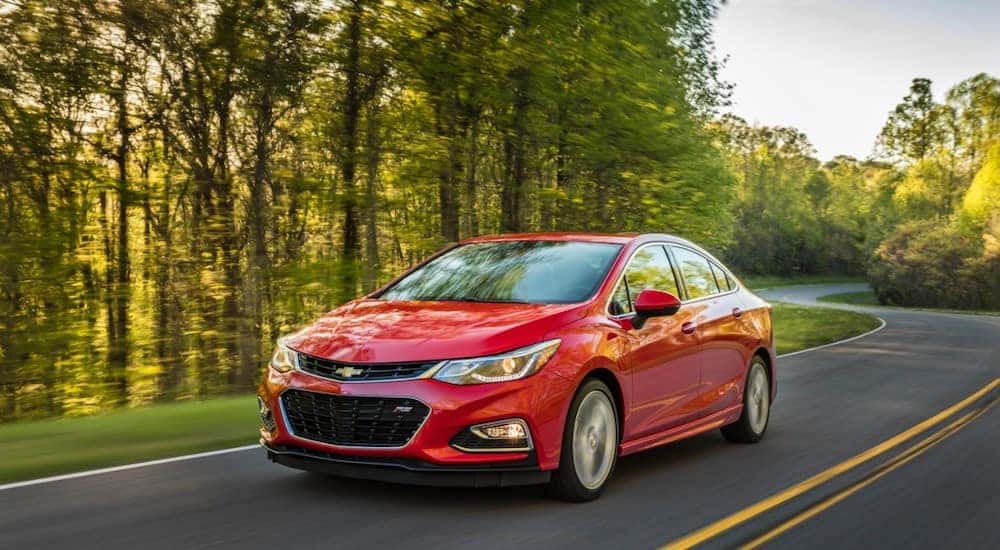 Red 2016 Chevrolet Cruze sedan on a paved road next to tall green trees
