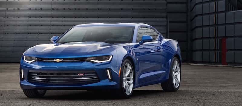 Front view of a blue 2016 Chevy Camaro parked outside a black building