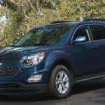Blue 2016 Chevrolet Equinox SUV parked on pavement in front of green trees