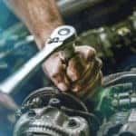 Hands of a mechanic working under the open hood of a vehicle