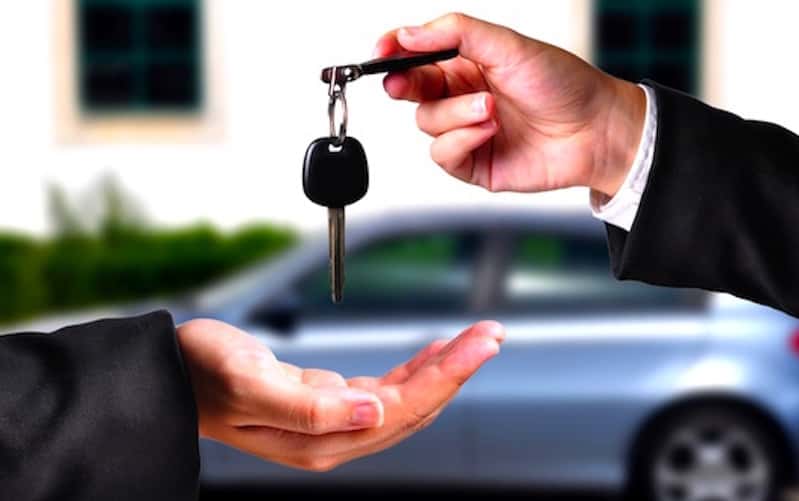 Hands exchanging keys in front of a silver sedan