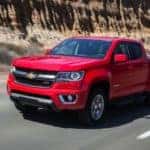 Red 2015 Chevrolet Colorado pickup truck on a paved road next to a tall brown dirt wall