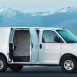 White 2016 Chevrolet Express Cargo Van parked with the backseat doors open in front of tall, snowy mountains