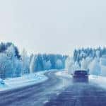 Car driving down a paved road next to snowy trees