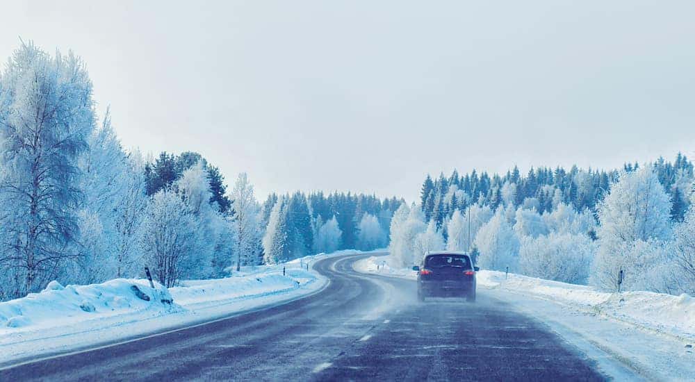 Car driving down a paved road next to snowy trees