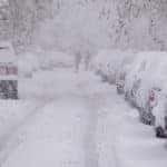 Cars covered in snow and parallel parked on the sides of a snowy road