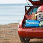 Open trunk of a red vehicle parked in front of water revealing a trunk full of luggage