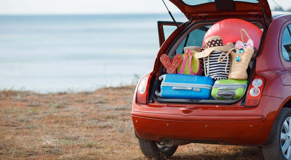 Open trunk of a red vehicle parked in front of water revealing a trunk full of luggage