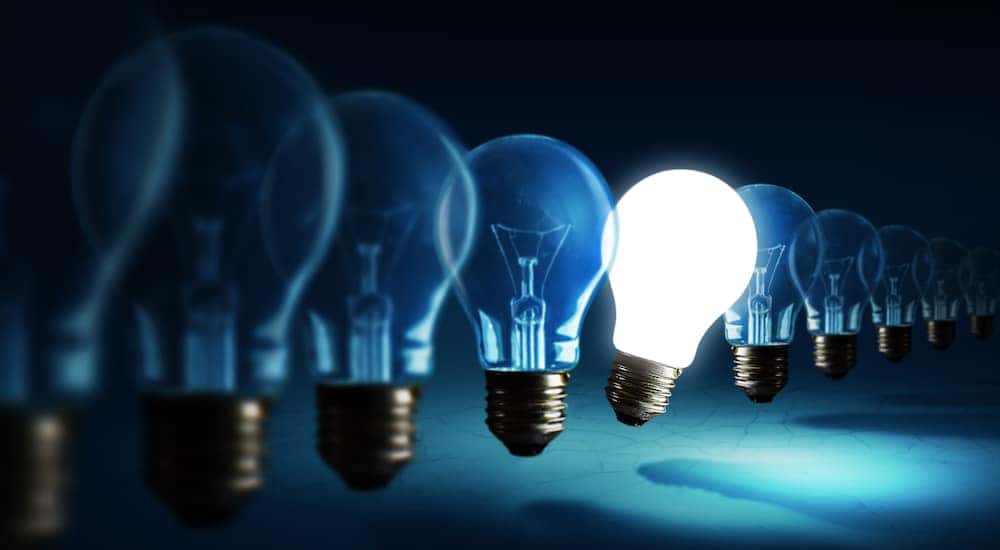 Line of lightbulbs hovering over a surface with one near the middle lit up