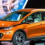 Man in a suit standing next to an orange 2017 Chevrolet Bolt hatchback