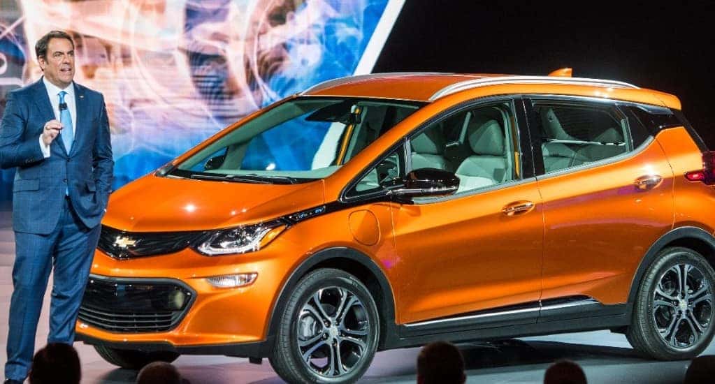Man in a suit standing next to an orange 2017 Chevrolet Bolt hatchback