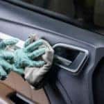 Hands in blue gloves using a rag and clear spray bottle to clean in interior of an open car door