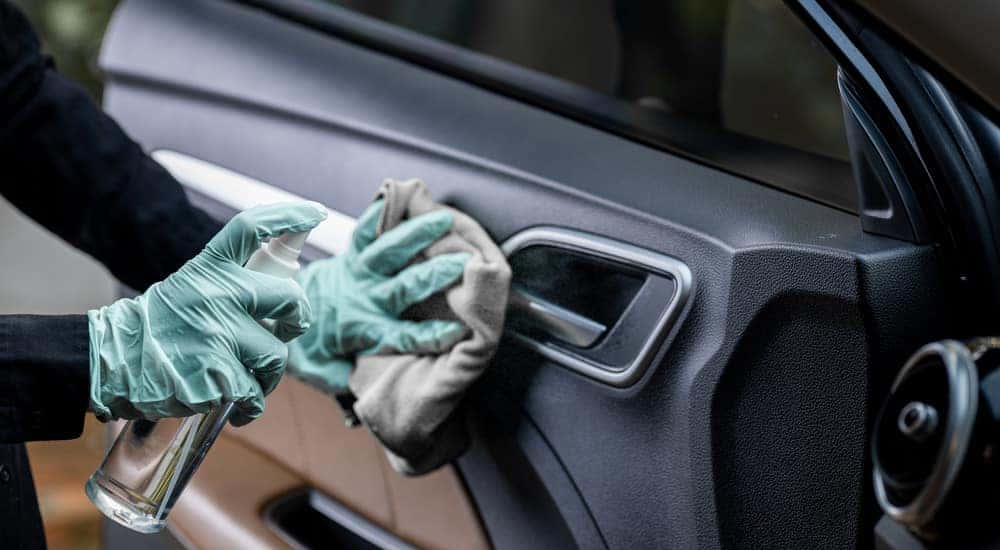 Hands in blue gloves using a rag and clear spray bottle to clean in interior of an open car door