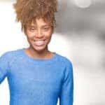 Woman in a blue sweater holding up three fingers in front of a blurred background