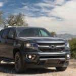 Black 2016 Chevrolet Colorado parked on a dirt road in front of trees with mountains in the background