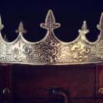 Gold king's crown sitting on top of a brown briefcase in a dark room