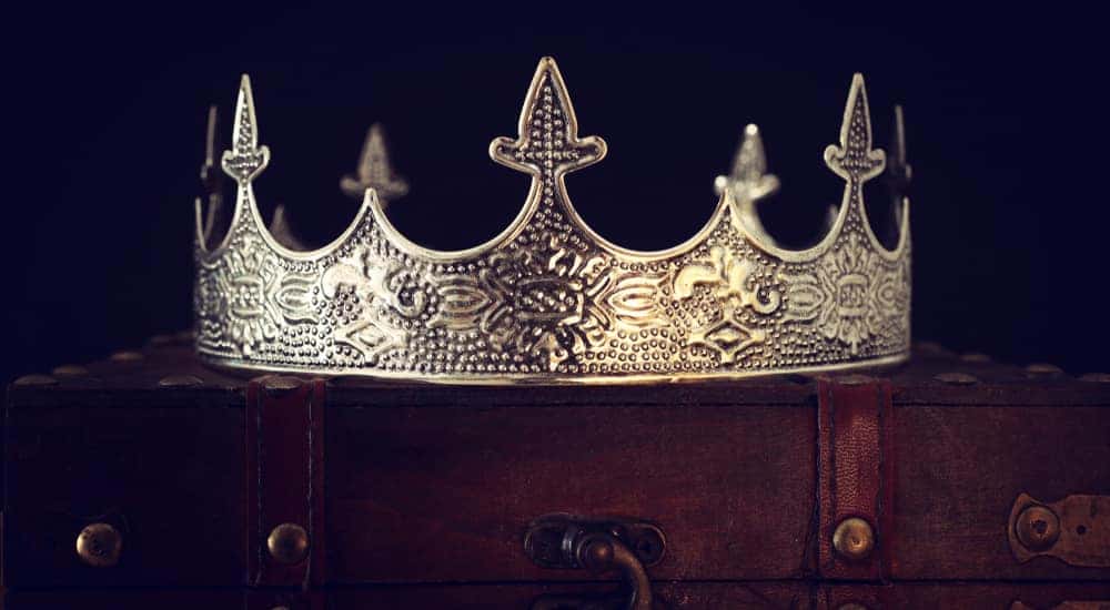 Gold king's crown sitting on top of a brown briefcase in a dark room