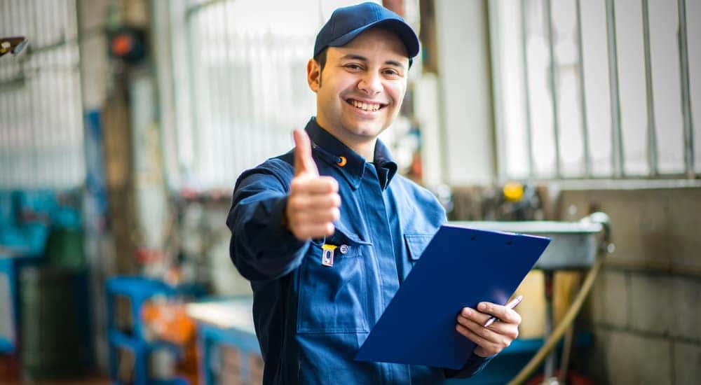 Mechanic in a blue jumpsuit and hat holding a clipboard and pen while giving a thumbs up