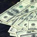 One hundred dollar bills spread out on a dark wooden table
