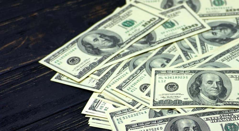 One hundred dollar bills spread out on a dark wooden table
