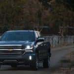Dark colored 2016 Chevrolet Silverado pickup truck driving through a metal gate on a dirt path