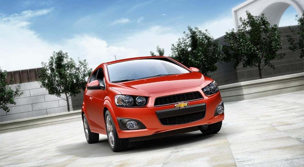 Orange 2016 Chevrolet Sonic parked in an empty lot with trees in the background