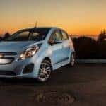 Baby blue 2016 Chevrolet Spark parked near a ledge in front of the sun setting behind a mountain
