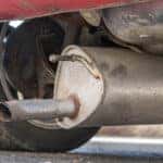 Car exhaust that has fallen off of the correct position on a red car