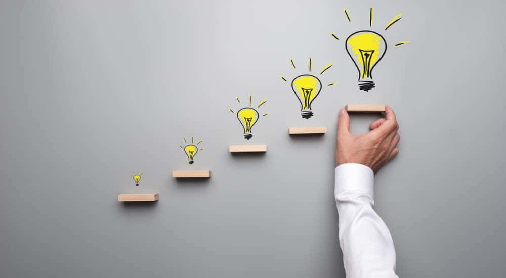 Five small wooden shelfs on a grey wall with yellow lightbulbs drawn above each one
