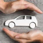 Hands protecting a paper car that is sitting on a grey table