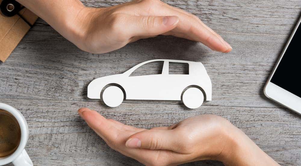 Hands protecting a paper car that is sitting on a grey table