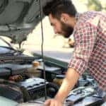 Man in a red plaid shirt leaning over the open hood of a vehicle