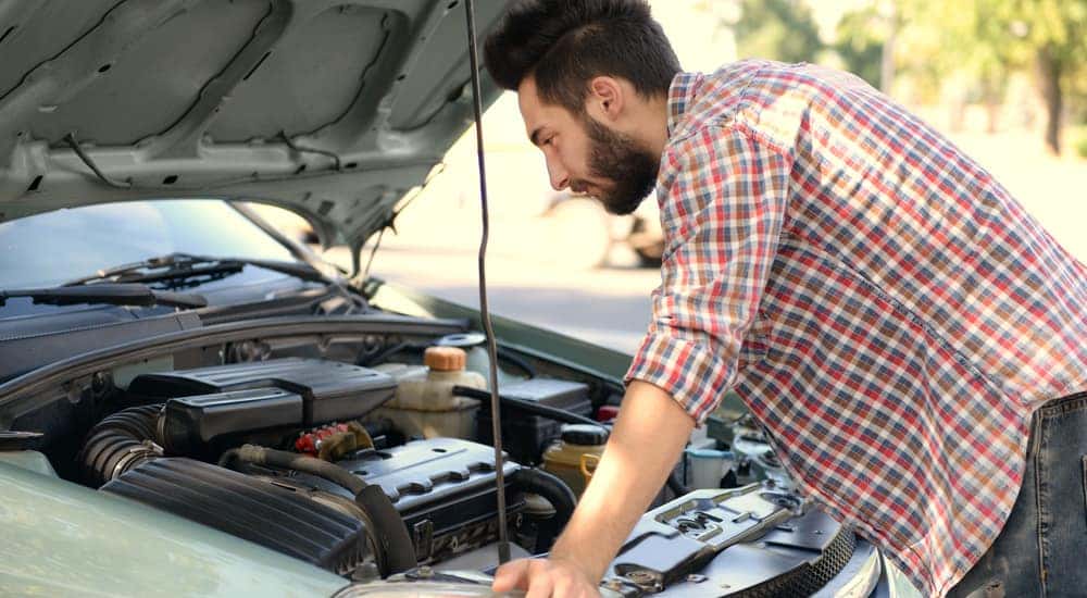 Man in a red plaid shirt leaning over the open hood of a vehicle