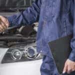 Man in a black suit shaking hands with a mechanic in all-blue clothing in front of a white vehicle