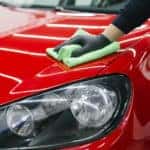Person in black gloves using a green cloth to professionally clean a red vehicle