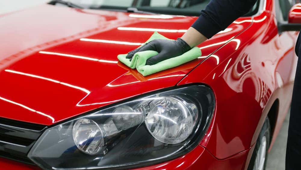 Person in black gloves using a green cloth to professionally clean a red vehicle