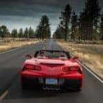 Red 2016 Chevrolet Corvette convertible performance vehicle driving down a paved road under a dark sky