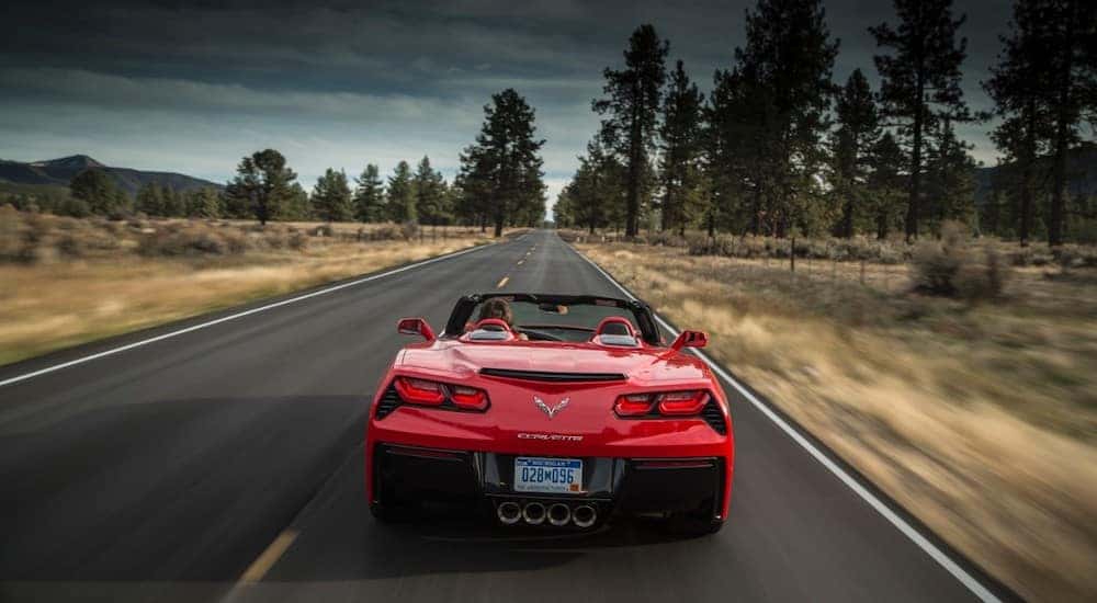 Red 2016 Chevrolet Corvette convertible performance vehicle driving down a paved road under a dark sky