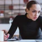 Woman in a black shirt looking intently at a white laptop while writing with a black pen