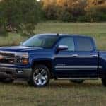 Blue 2014 Chevrolet Silverado pickup truck parked in a grass field in front of green trees