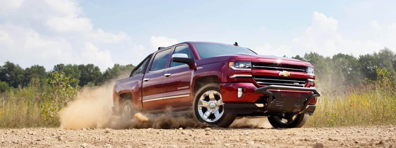 A red 2016 Chevy Silverado is kicking up sand on a dirt road near Albany, NY.