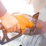 Hand holding an orange gas pump in the gas tank of a vehicle