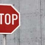 Red and white stop sign on a silver post in front of a cement wall