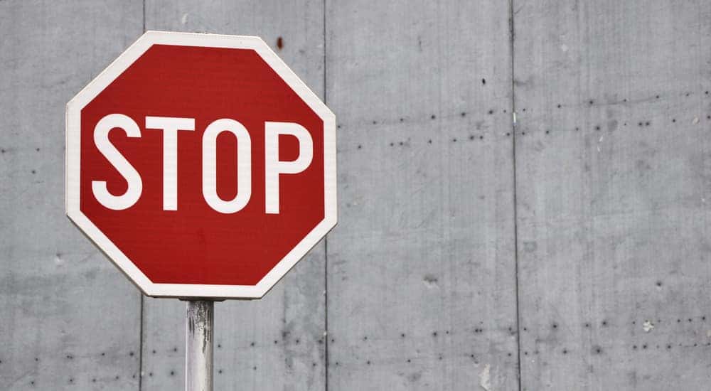 Red and white stop sign on a silver post in front of a cement wall