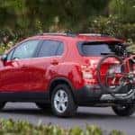 Red 2016 Chevrolet Trax SUV with bikes hooked on the back driving down a paved street