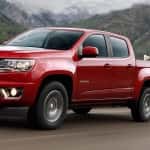 A red 2016 Chevy Colorado is towing dirt bikes on a mountain road.