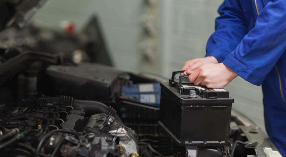 Man in a blue jumpsuit holding onto a car battery that is lifted out of a vehicle's open hood