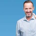 Man in a blue button-up shirt holding up five fingers in front of a blue wall